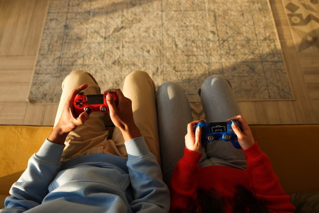 Two individuals using game controllers while sitting on a yellow couch, focused on gaming.